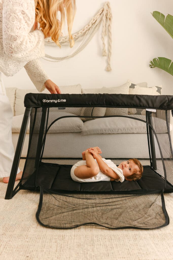 Baby sleeping in a lightweight travel crib in a sunlit hotel room