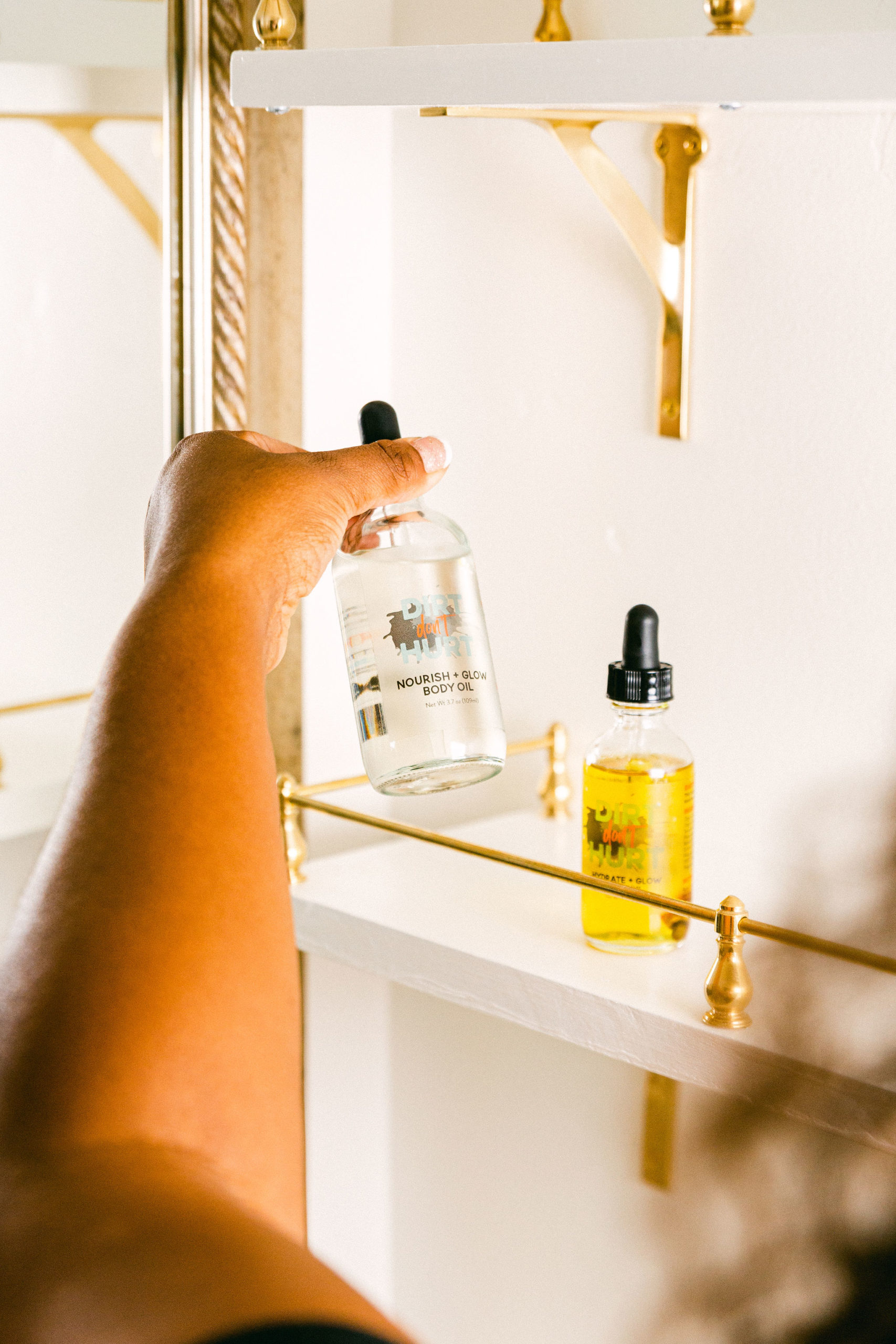 Natural skincare product photography black woman picking up body oil from bathroom shelf