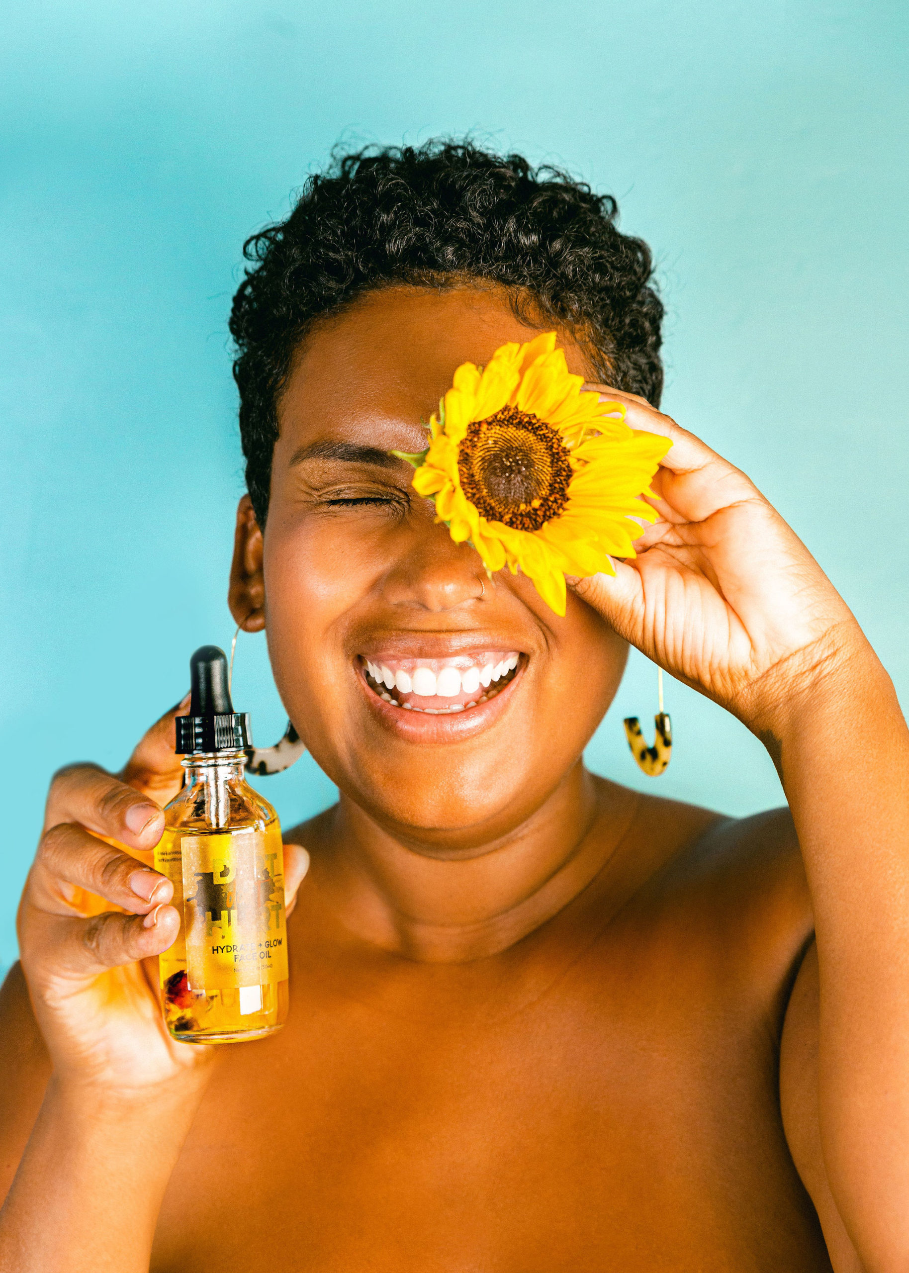 Black Women Sunflower Skincare oil product photography natural smiling cheerful fun funky product photography turquoise backdrop