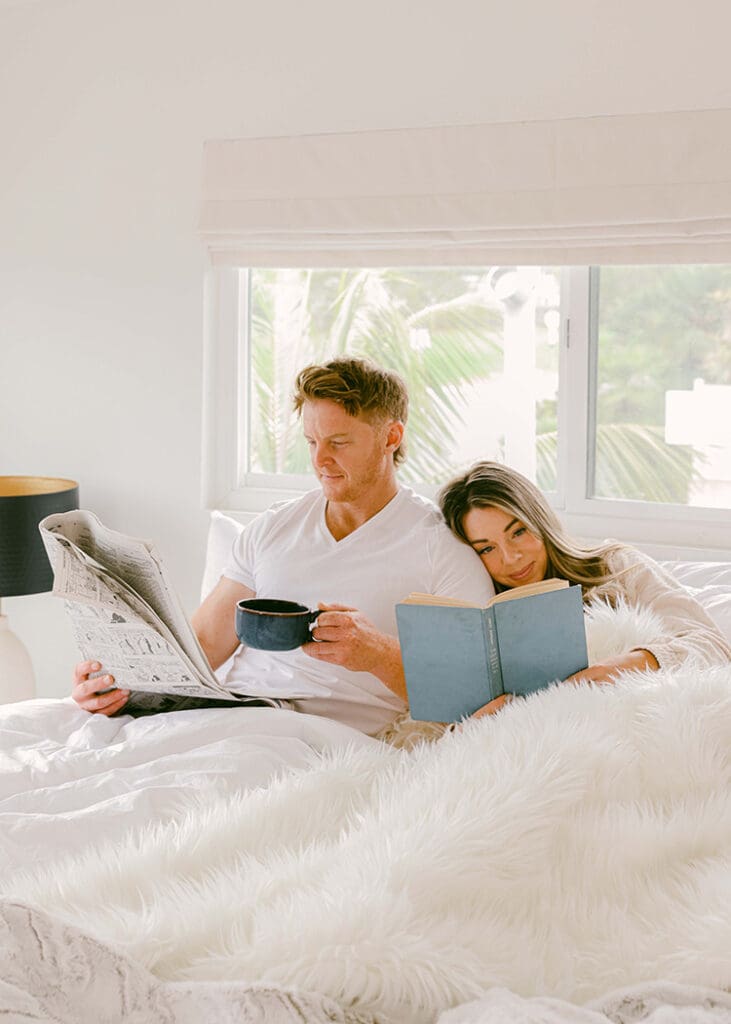 A couple cuddling in bed on a morning reading a newspaper and drinking coffee lifestyle airbnb photography