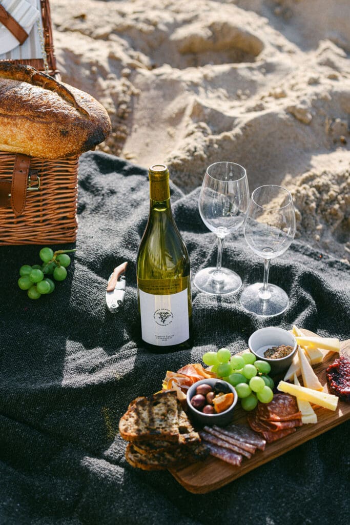 girl drinking glass of wine on beach monterey california - boutique hotel photography picnic on the beach with wine cheese charcuterie baguette