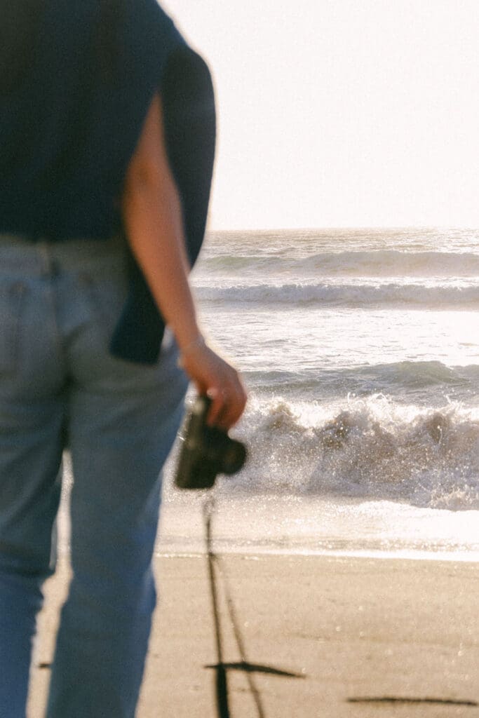 free spirited girl on the beach ocean posh sweater over shoulders golden hour california vibes sunny vintage camera