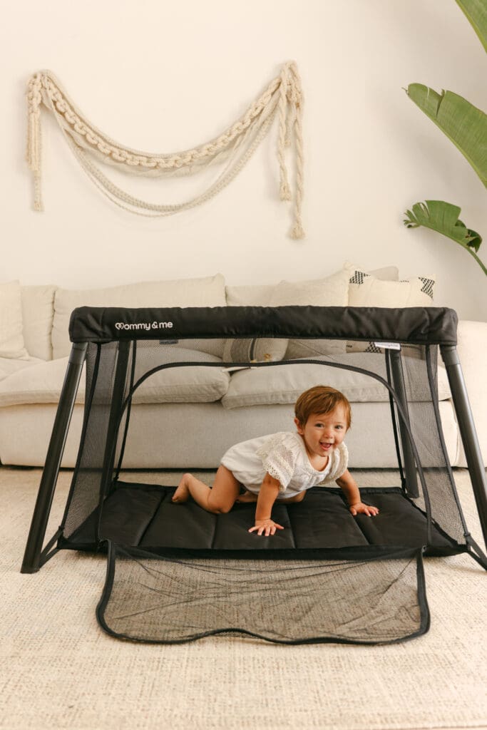 Baby crawling in a lightweight travel crib in a sunlit hotel room