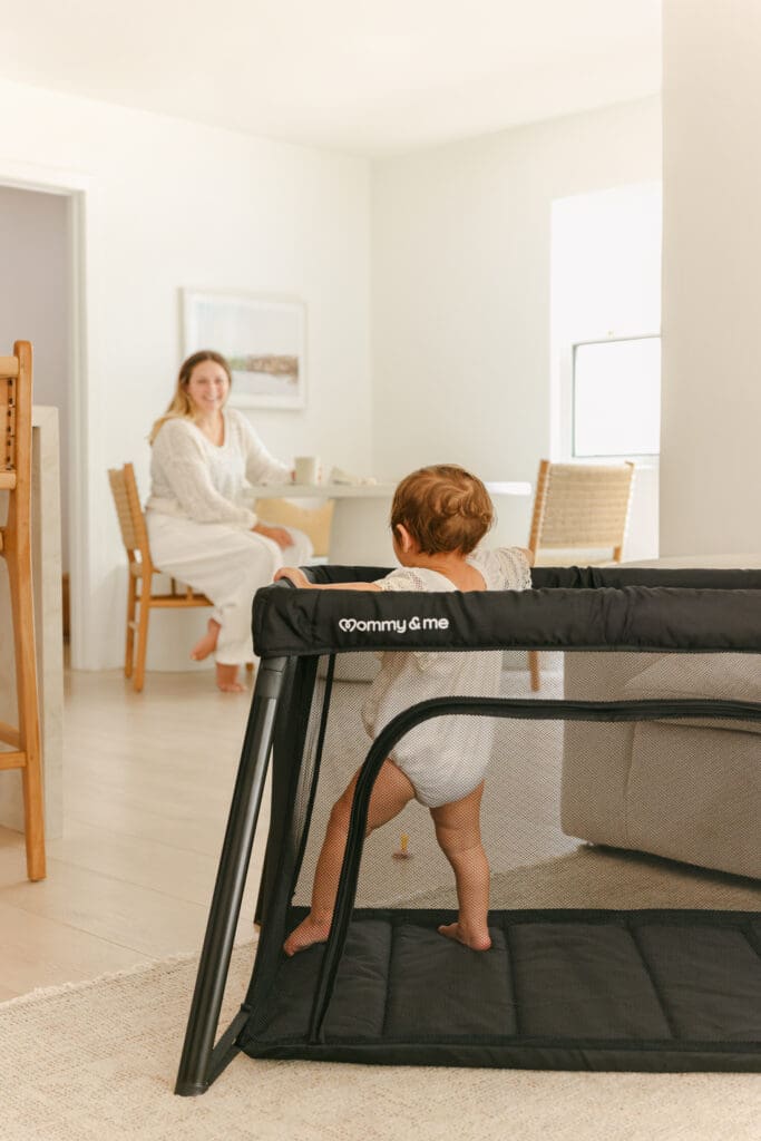 mom drinking coffee and baby in a lightweight travel crib in a sunlit hotel room
