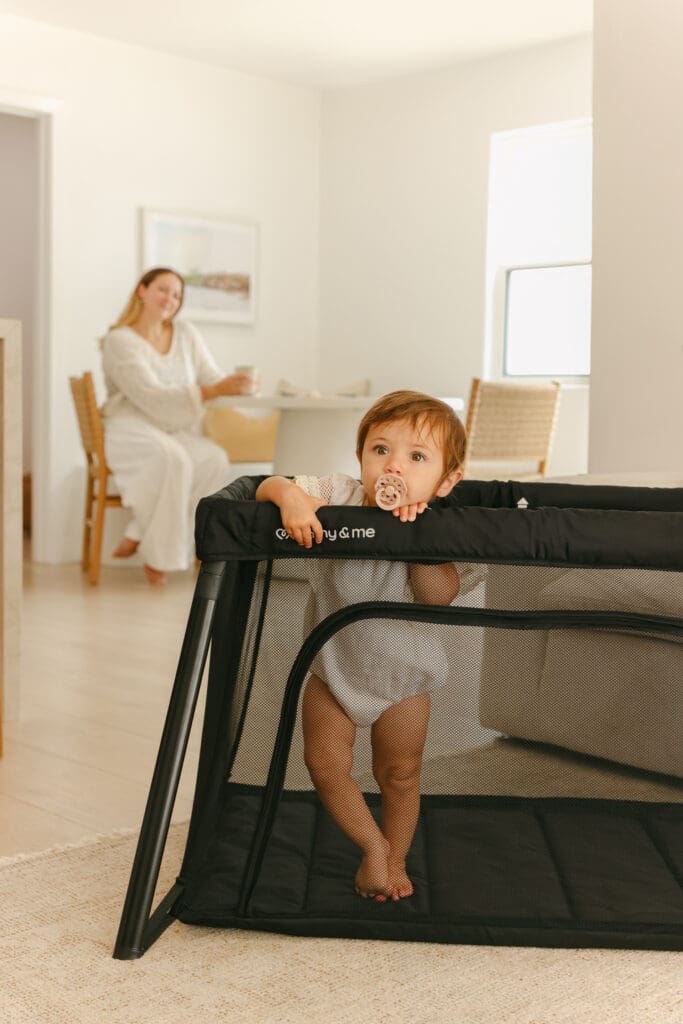 mom drinking coffee and baby in a lightweight travel crib in a sunlit hotel room