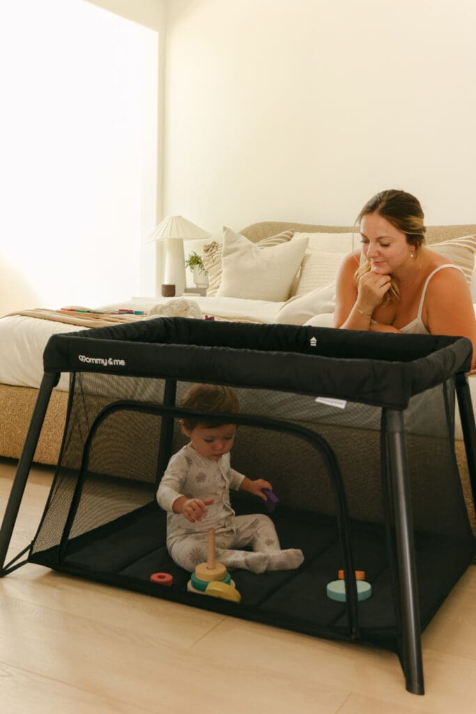 Baby playing with blocks in a lightweight travel crib in a sunlit hotel room