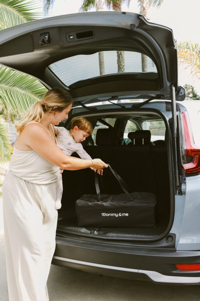 putting travel crib in car with baby and mom backseat