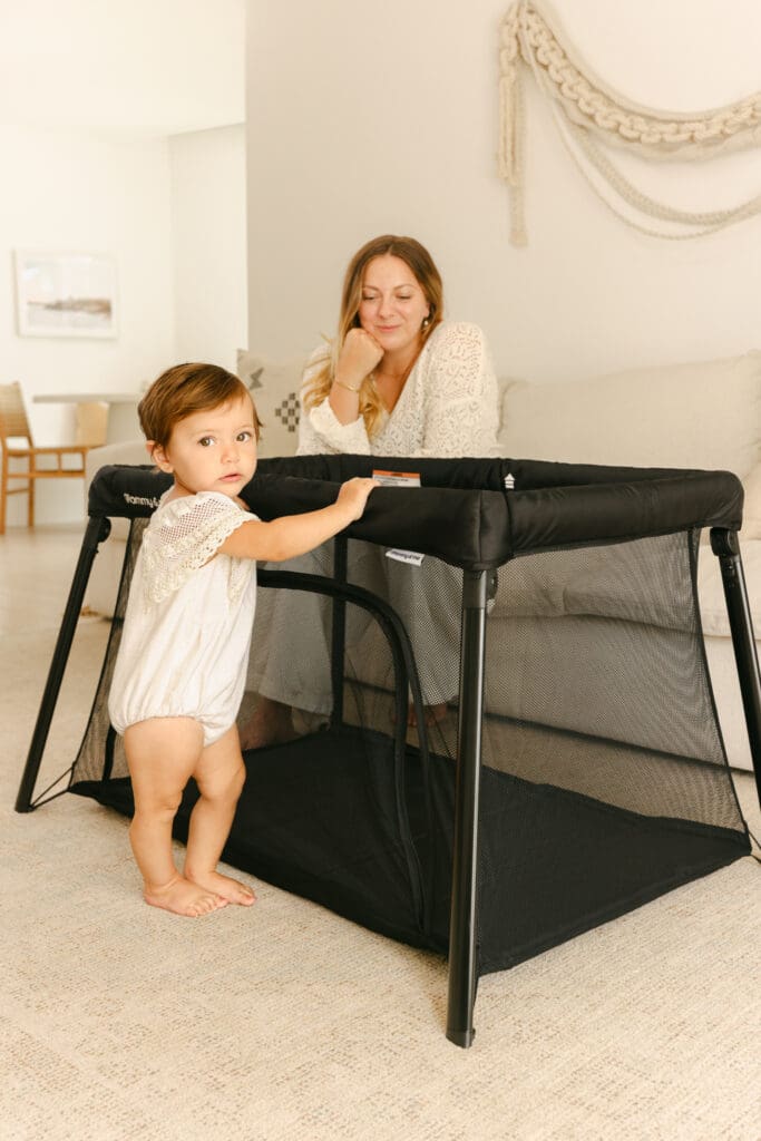 Baby playing in a lightweight travel crib in a sunlit hotel room natural