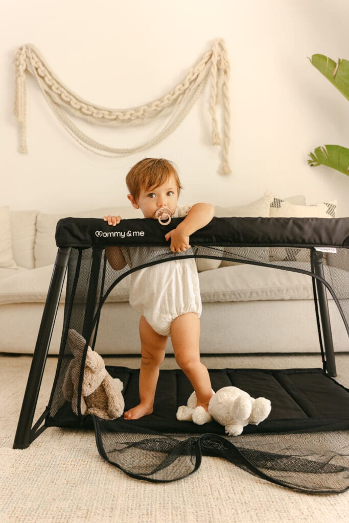 Baby with stuffed animals playing in a lightweight travel crib in a sunlit hotel room natural