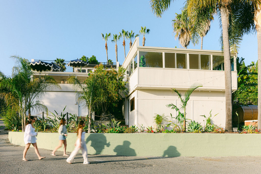 Three women walking past the exterior of Tide Haus, a luxury Airbnb vacation rental surrounded by tropical palms in Carlsbad, California, photographed by Chelsea Loren
