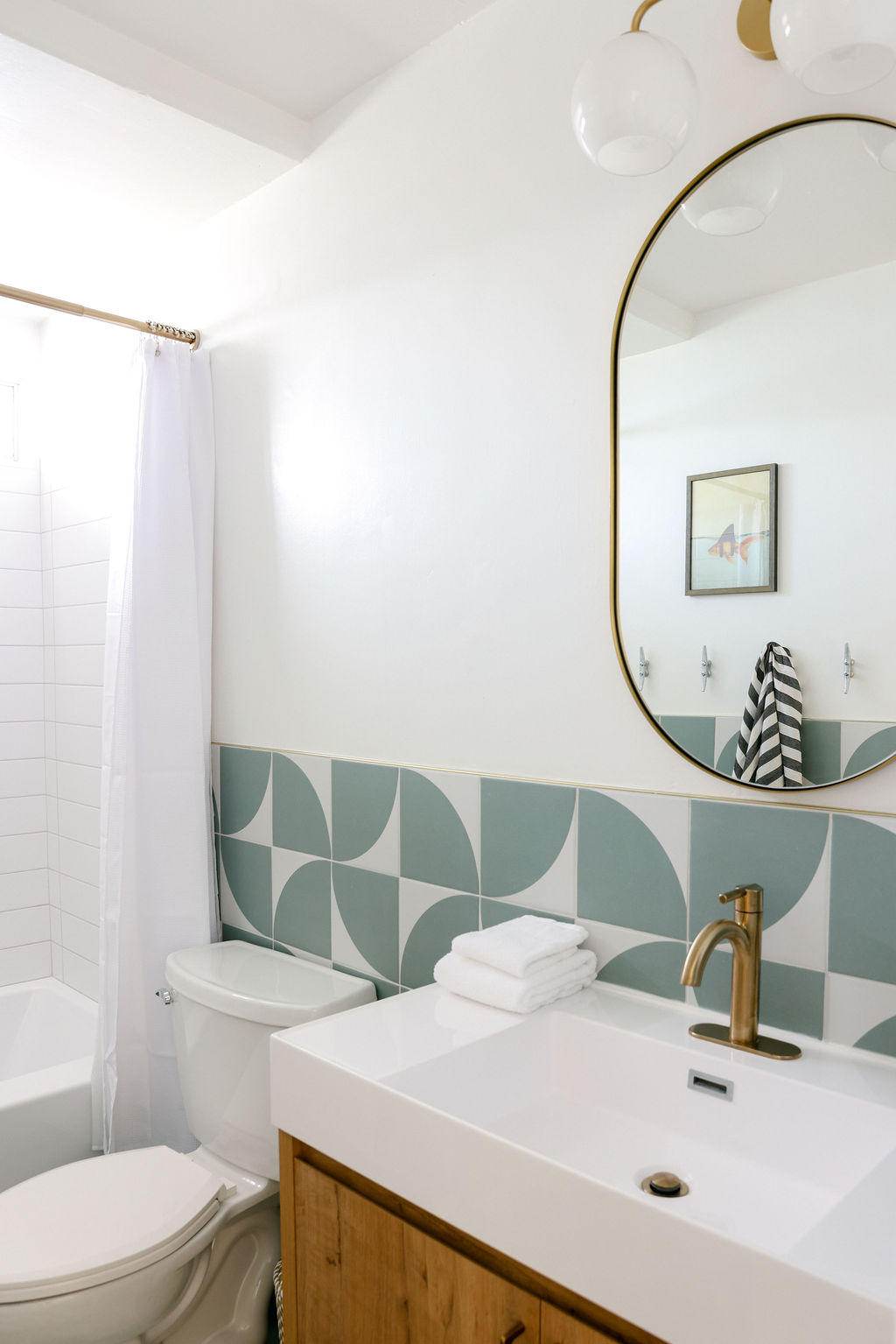 Boutique Airbnb bathroom with white subway tile shower, gold fixtures, teal geometric floor tiles, and striped Turkish towel in Carlsbad, California, photographed by Chelsea Loren