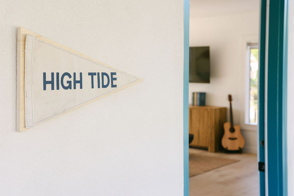 Bright boutique Airbnb bedroom with rattan pendant light, crisp white bedding, woven rug, and playful No Wake Zone wall sign in Carlsbad, California, photographed by Chelsea Loren