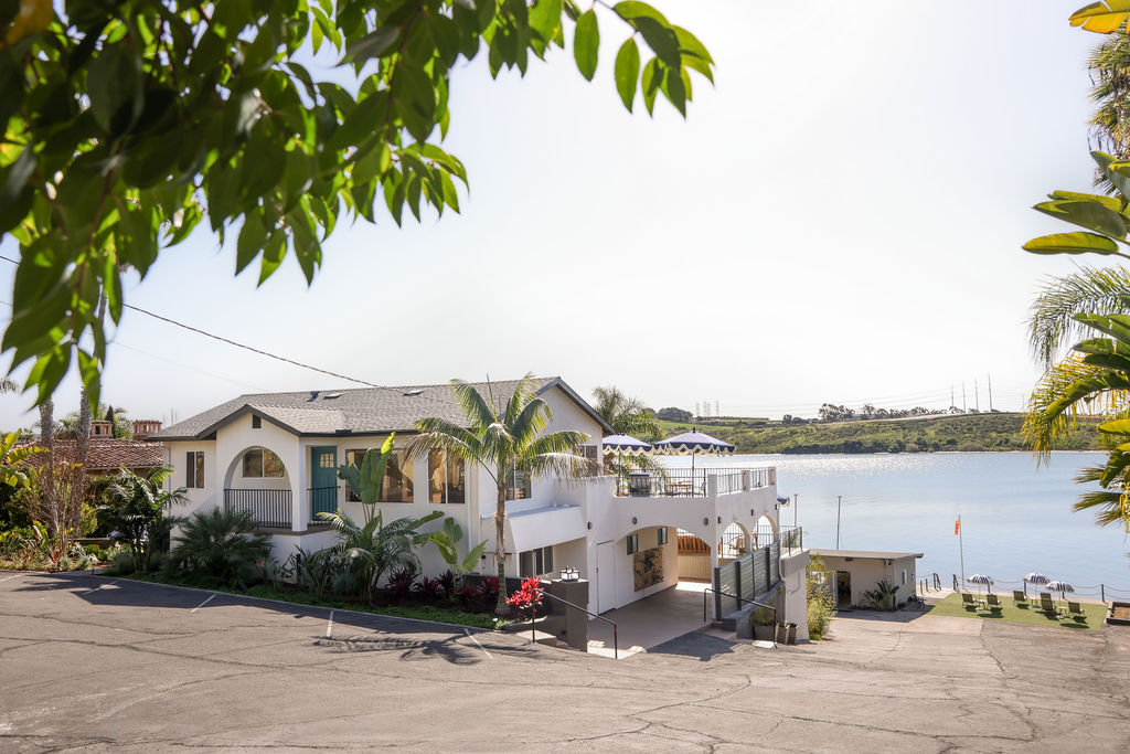 Person paddleboarding on the calm Carlsbad Lagoon with luxury lounge chairs and striped beach umbrellas at a waterfront Airbnb in Southern California, photographed by Chelsea Loren