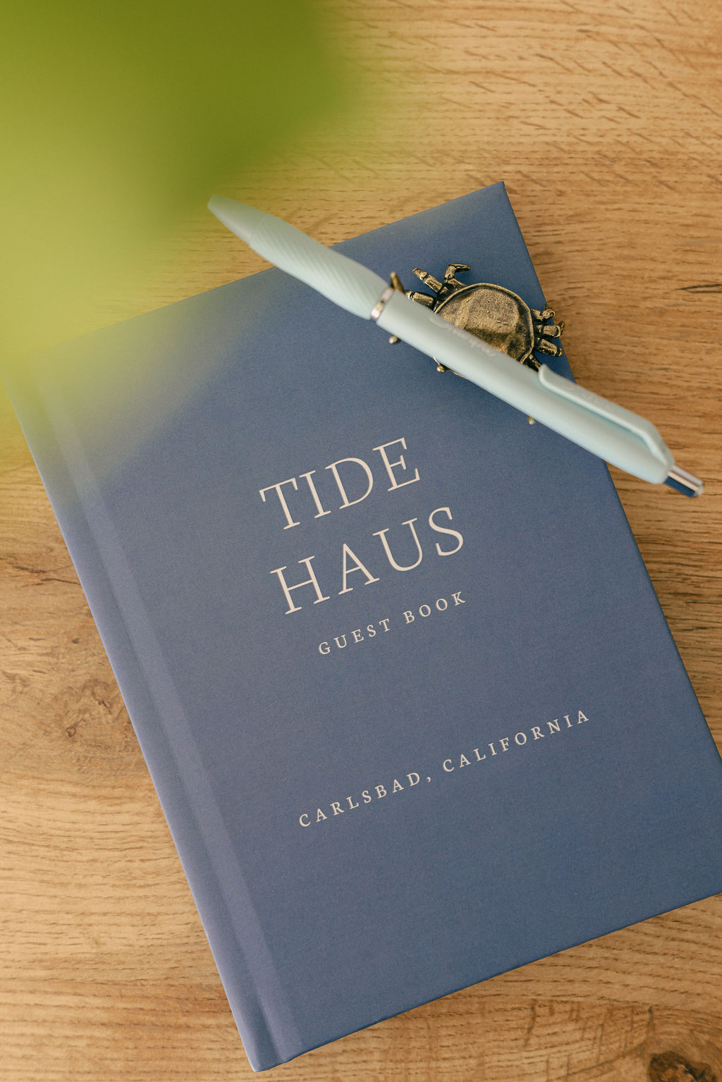 Tide Haus guest book in navy with gold lettering reading Carlsbad California on a wood table at a luxury Airbnb vacation rental, photographed by Chelsea Loren