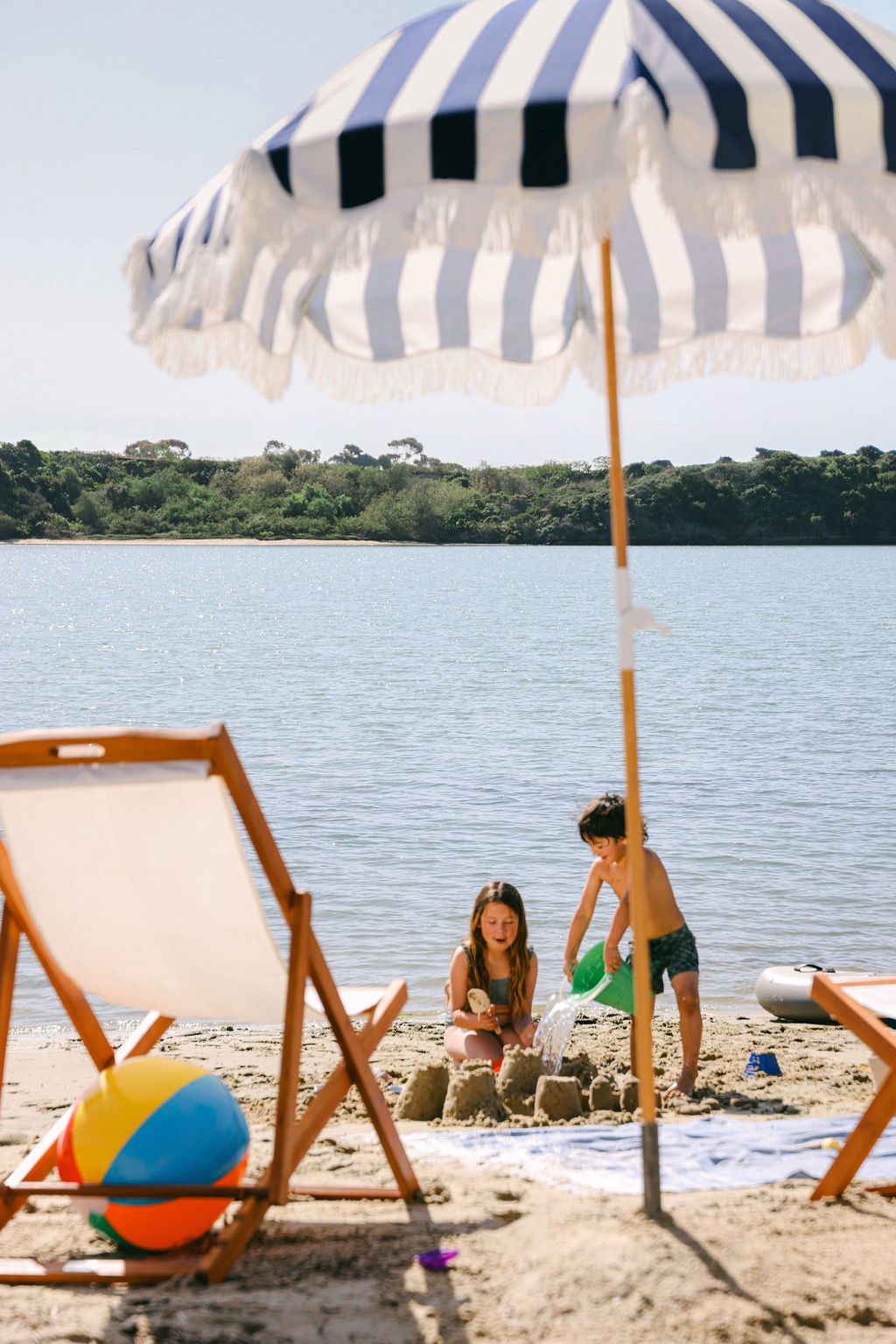 Children playing on the sandy shore of Carlsbad Lagoon with beach chairs and a colorful beach ball at a luxury Airbnb in Southern California, photographed by Chelsea Loren