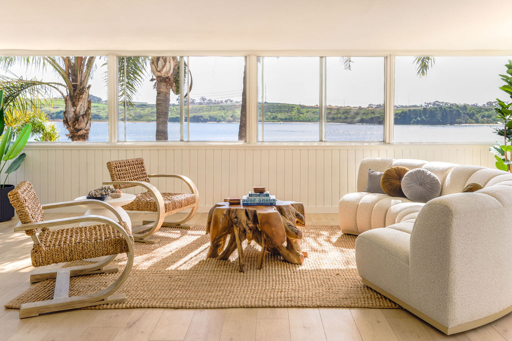 Sunlit Airbnb living room with cream sectional sofa, rattan lounge chairs, and sweeping Carlsbad Lagoon and palm tree views, photographed by Chelsea Loren