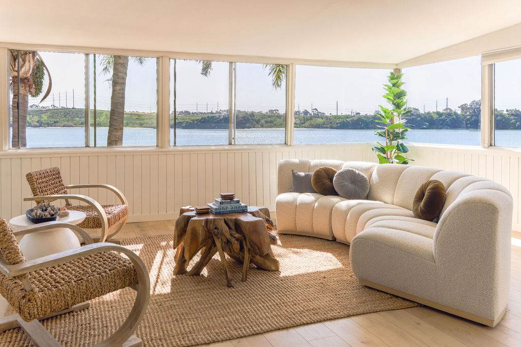 Luxury Airbnb living room with cream bouclé sectional sofa, natural wood coffee table, and panoramic Carlsbad Lagoon views, photographed by Chelsea Loren