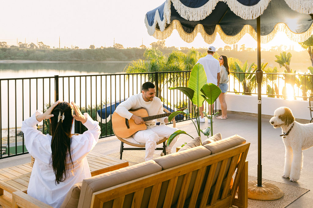 Luxury rooftop lifestyle photography at the Carlsbad lagoon, man playing guitar while guests dance and enjoy panoramic lagoon views at golden hour, by Chelsea Loren