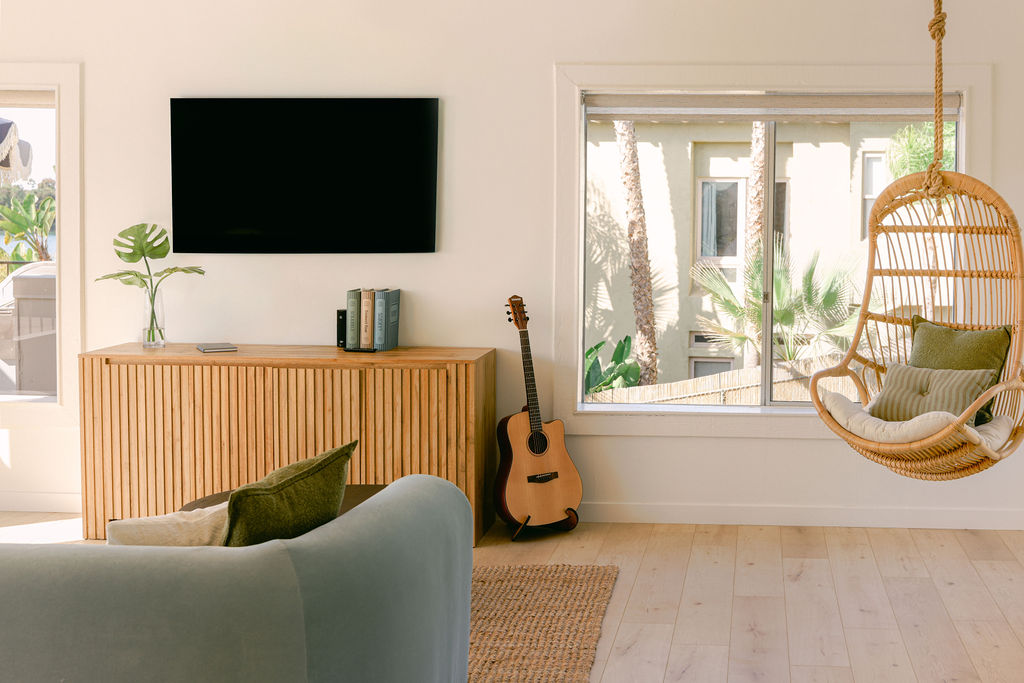 Wide-angle view of a luxury Airbnb open plan living and dining area with lagoon views, acoustic guitar, hanging rattan chair, and wood furniture in Carlsbad, California, photographed by Chelsea Loren