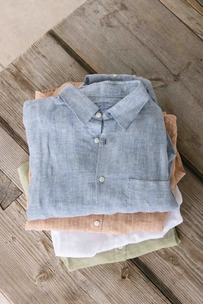 MUJI linen shirts stacked on weathered wood surface in quiet editorial product photography style