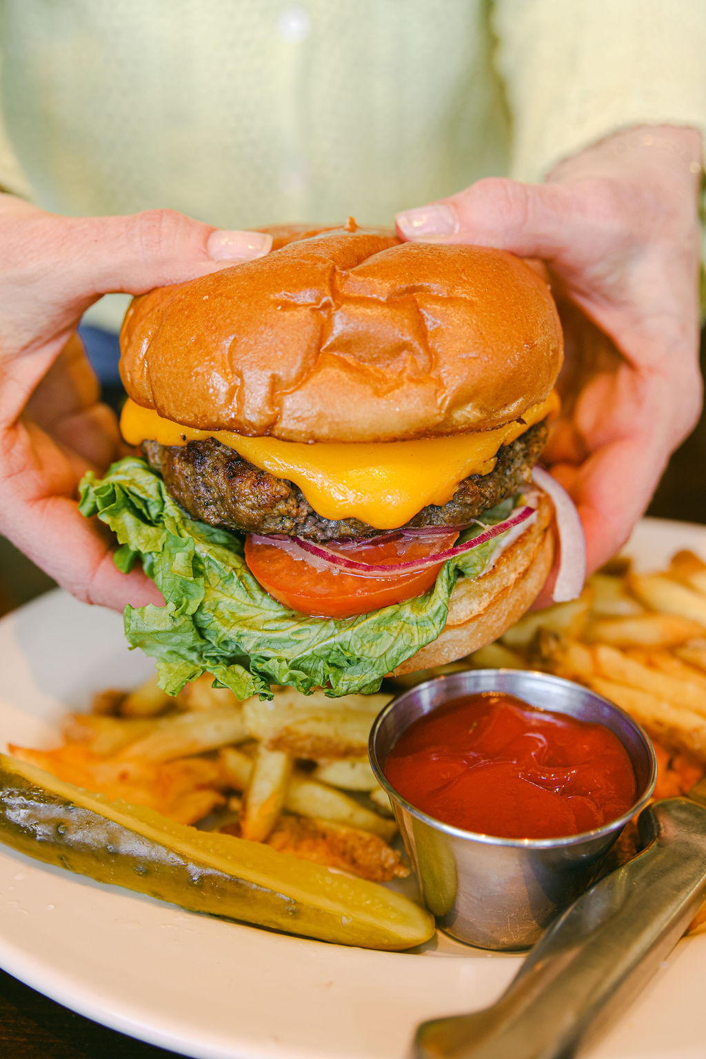Hands holding a towering cheeseburger with all the fixings at MooMoo's Burger Barn in Lodi California
