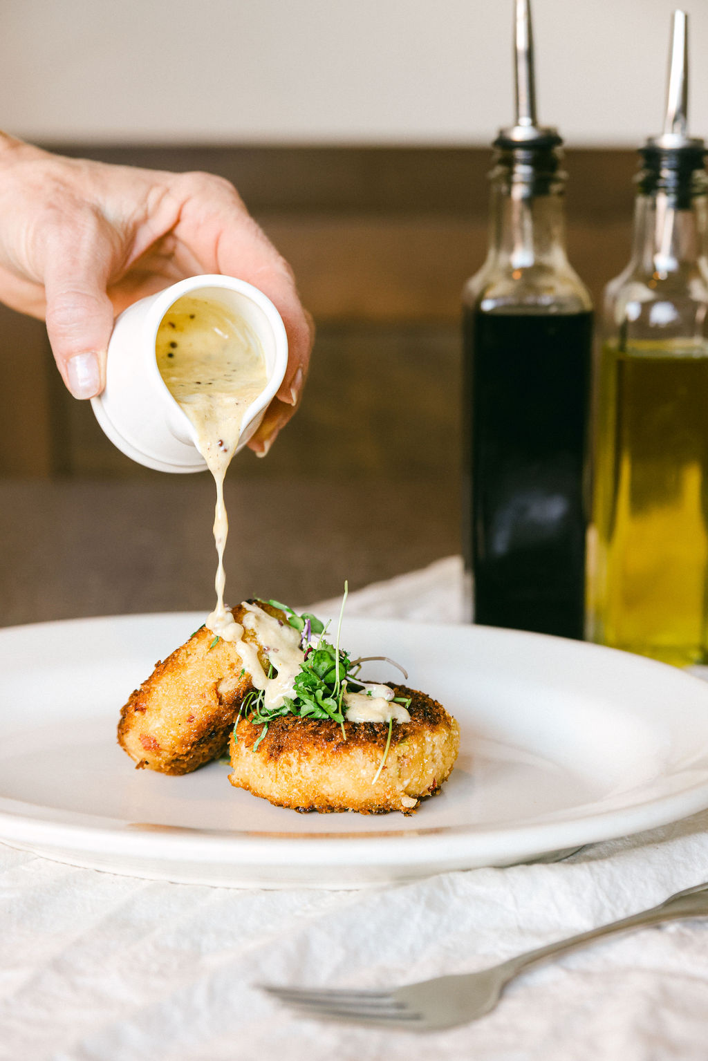 Sauce being poured over a beautifully plated fried cake with microgreens at Papapavlo's Bistro Lodi