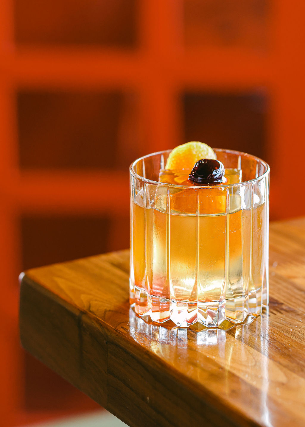 Three craft cocktails on warm wood bar - old fashioned, red coupe cocktail, and tall cucumber gin drink at The Oxford Kitchen Lodi