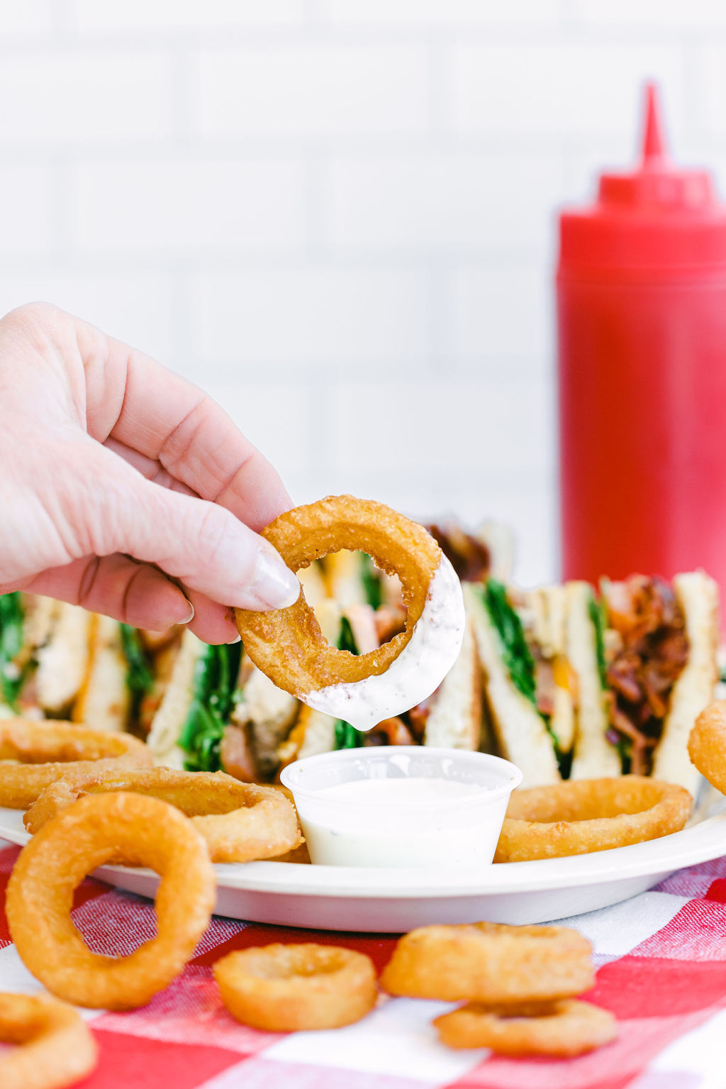 Hand dipping onion ring into ranch dressing with club sandwich in background at MooMoo's Burger Barn Lodi