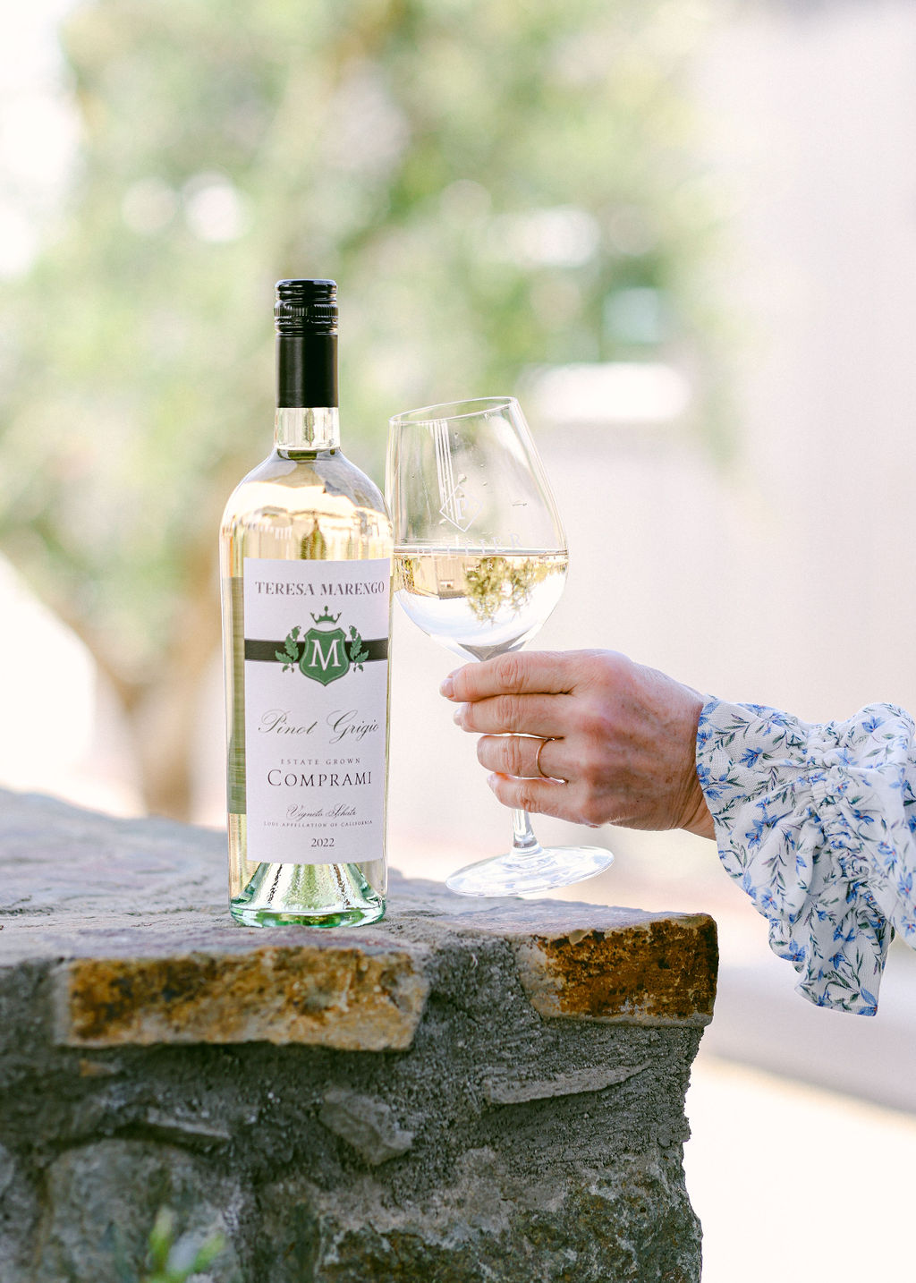 Close-up of Peltier Winery branded wine glass with white wine and woman in blue floral blouse in background
