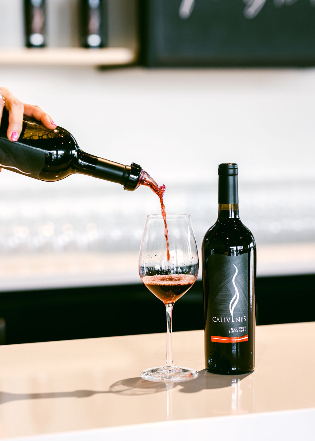 Calivines Old Vine Zinfandel being poured into glass in sleek modern white tasting room in Lodi California