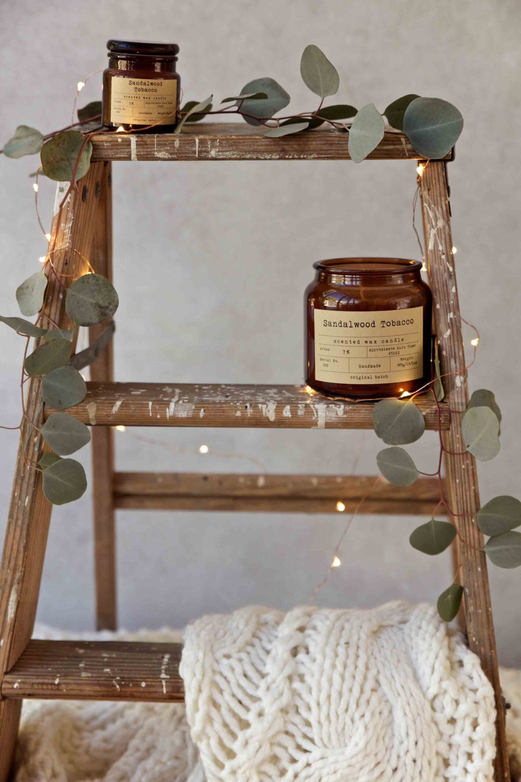 Styled candle product on rustic wood shelf with eucalyptus and warm string lights showcasing texture and atmosphere